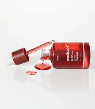 A bottle of Medicube EGF NAD Firming Serum lying on its side beside a drop of serum, illustrating an article on what skin longevity means